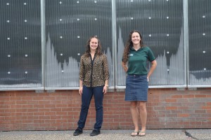 Ellen Vaughan, right, manager of NAU's Office of Sustainability, and Jessica Lazor, chair of the student-run Green Fund, stand in front of panels using solar thermal energy to heat a warehouse on campus. (Photo by Samantha Witherwax/Cronkite News)