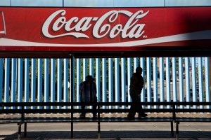 A man and boy wait for the bus in front of the border wall in Nogales, Sonora. (Photo by Courtney Pedroza/Special for Cronkite News)