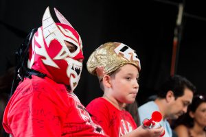 Two fans in masks watch luchadores in the ring. (Photo by Christopher West/Cronkite News)