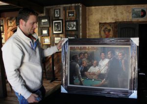 Dan Lohmeier, co-owner of Far From Folsom on Whiskey Row in Prescott, holds up a painting of Republican presidents. (Photo by Kia Murphy/Cronkite News)