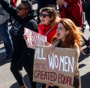 Three women marching side-by-side in solidarity for women around the globe. (Photo by Saeed Alshamisi/Cronkite News)