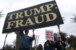 Phoenix resident Chris Fleischman, 54, stands with a large sign that reads “TRUMP: FRAUD” in front of the Arizona State Capitol on Friday, January 20, 2017. The gathering was in protest of the inauguration of President Donald Trump. (Photo by Ryan Santistevan/Cronkite News)