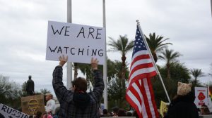 Several hundred people protested the inauguration of President Donald Trump at the Arizona State Capitol on Friday, Jan. 20, 2017. One protester held handmade sign that read “WE ARE WATCHING.” (Photo by Ryan Santistevan/Cronkite News)