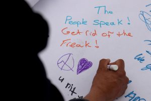 One protester draws a peace sign and a heart as a contribution to the hand-made poster. The sign was an activity for people at the inauguration protest at the Arizona State Capitol on Jan. 20, 2017. (Photo by Nicole Tyau/Cronkite News)